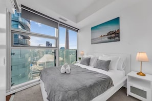 Habitación de hotel moderna con una cama grande, vista a un paisaje urbano y un cuadro en la pared.