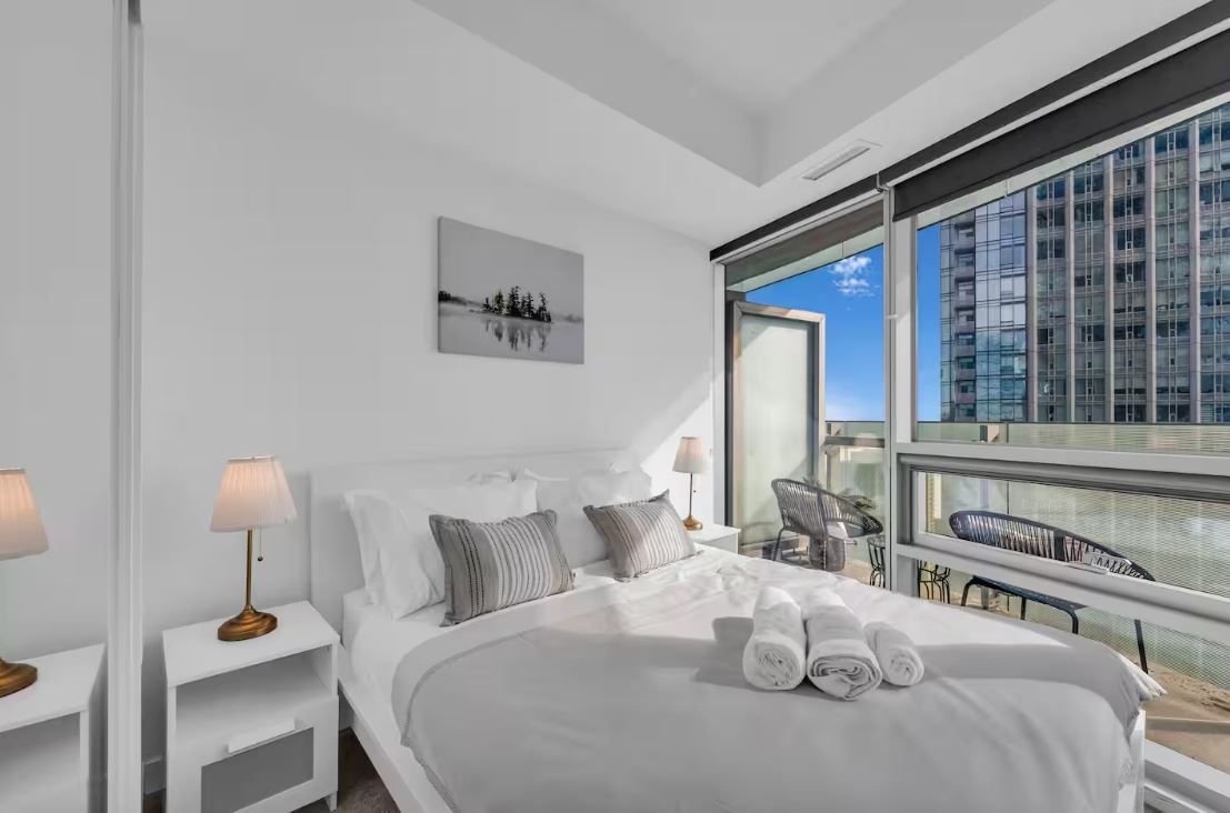 Een moderne hotelkamer met een groot bed, een nachtkastje, een lamp, een schilderij en een balkon met uitzicht op de stad.