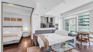 Una habitación de hotel moderna con una cama grande, una zona de estar independiente, una kitchenette y una mesa de comedor.