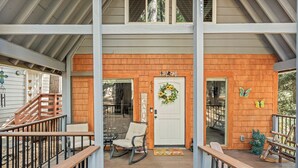 Un portico riparato con un patio in legno, una poltrona a dondolo, una panca e una porta con un cartello di benvenuto.
