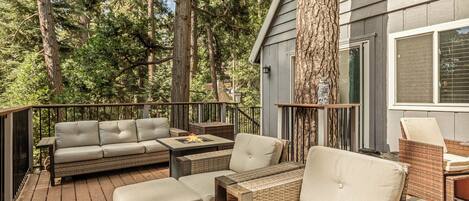 A deck with outdoor furniture, including sofas and a coffee table, surrounded by trees.