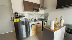 Cocina compacta con refrigerador, microondas, estufa y una pequeña isla con dispensador de agua.