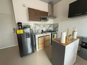 Eine kompakte Küche mit Kühlschrank, Mikrowelle, Herd und einer kleinen Kochinsel mit Wasserspender.