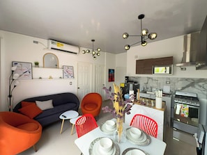 A modern living room with a sofa, chairs, a dining table set for two, and a kitchen area with a stove and microwave. - Entire Place: Residence in San Miguel, El Salvador (San Miguel)