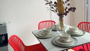 Un comedor con una mesa dispuesta para cuatro, sillas rojas, un florero con detalles decorativos y un televisor de pantalla plana montado en la pared.