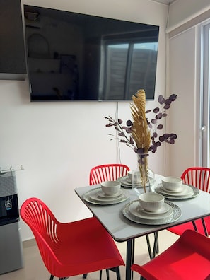 A dining area with a table set for four, red chairs, a vase with decorative elements, and a flat-screen TV mounted on the wall.