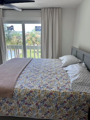 A bedroom with a bed, curtains, and a view of a balcony.