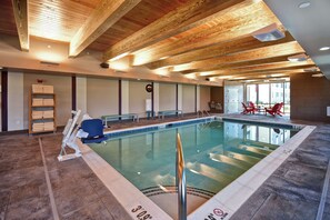 Una piscina interior con vigas de madera en el techo, un banco y un perchero.