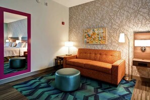 Habitación de hotel con sofá, reposapiés, lámparas, un espejo y un cuadro en la pared.
