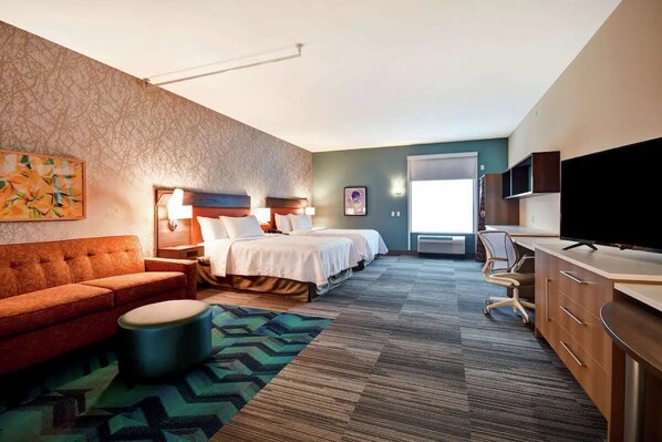 Una habitación de hotel con un sofá, dos camas, un televisor, un escritorio y una alfombra estampada.