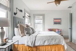 A bedroom with a bed, bedside lamps, a clock, a window with blinds, a ceiling fan, and a framed picture on the wall. - Historic Houston Midtown Haven (Houston)