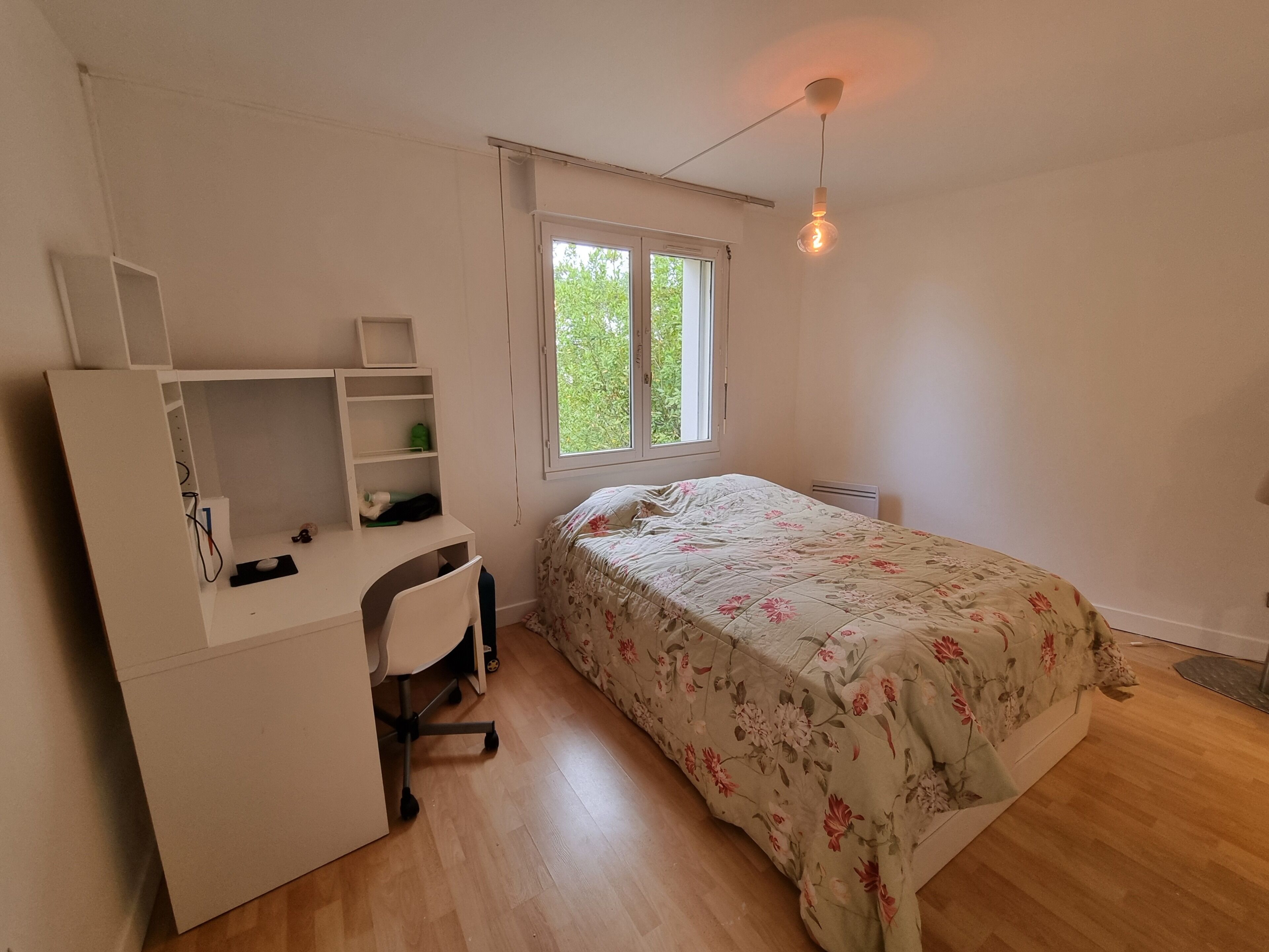 Une chambre à coucher comprenant un lit, un bureau, une chaise, une fenêtre et un luminaire suspendu.