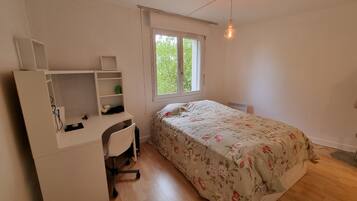 Une chambre à coucher comprenant un lit, un bureau, une chaise, une fenêtre et un luminaire suspendu.