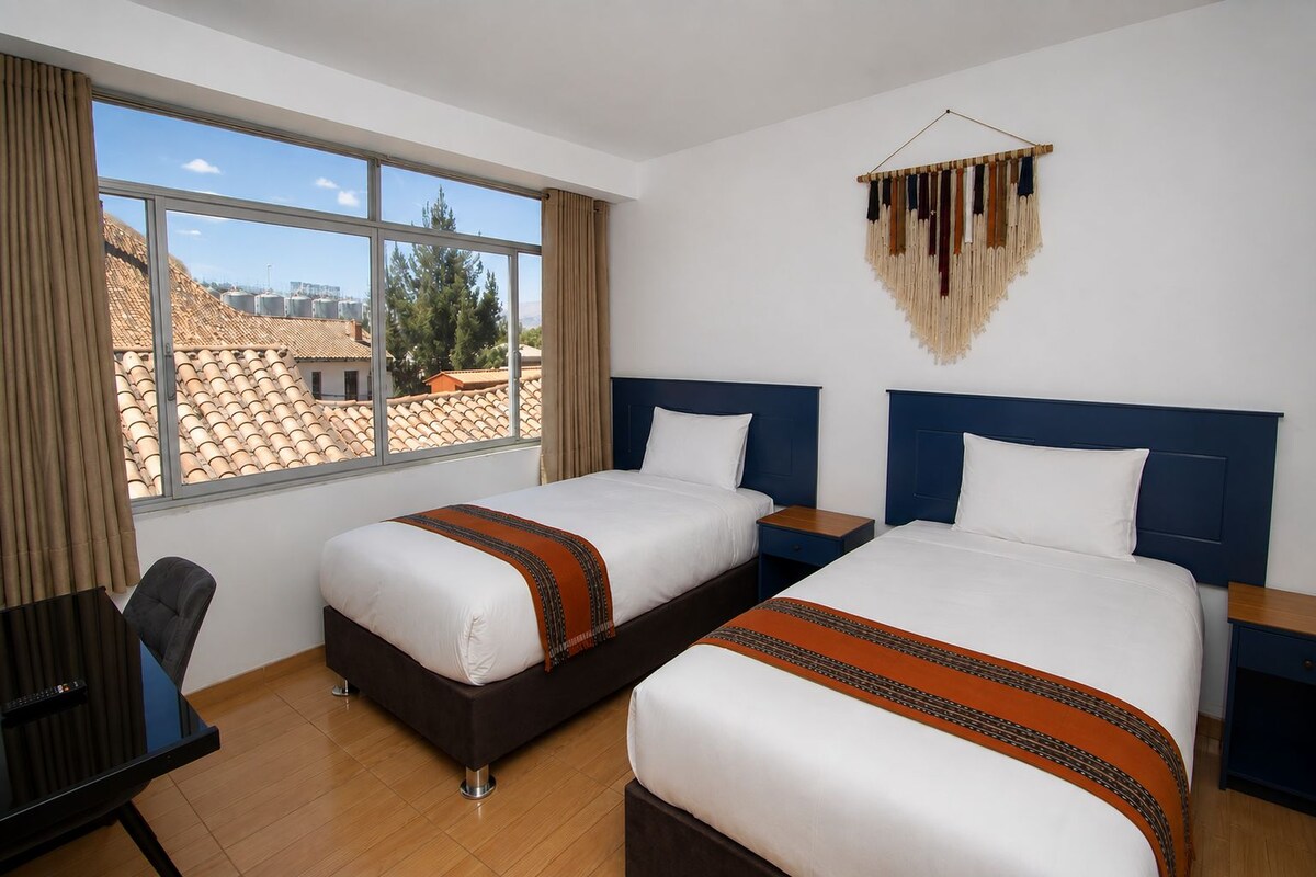 A hotel room with two beds, a desk, and a large window.