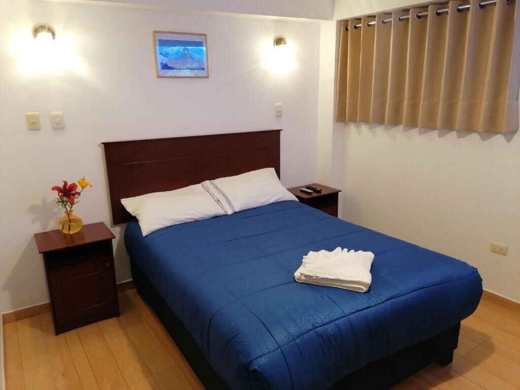 Hotelkamer met een bed, nachtkastje, lamp, foto aan de muur en raam met gordijnen.
