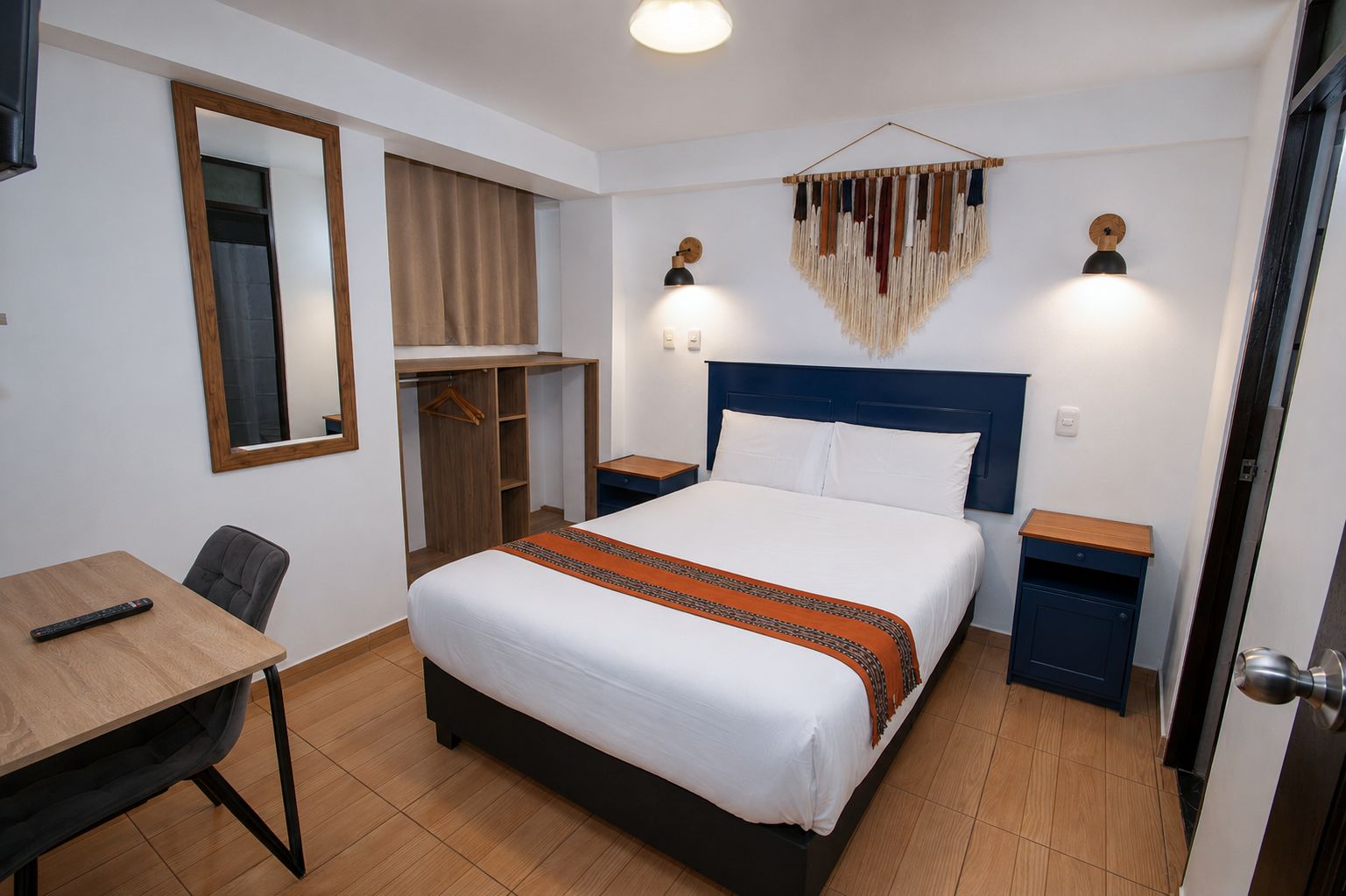 A hotel room with a bed, bedside tables, a desk, a chair, a wardrobe, and a mirror.
