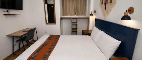 A hotel room with a bed, a desk, a chair, a TV, a lamp, and a wardrobe.