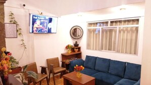 Una sala de estar con un sofá azul, una mesa de centro de madera y un televisor montado en la pared.