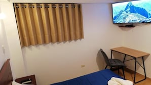 Habitación de hotel con cama, escritorio, silla, televisor y cortina.