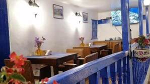 Interior de restaurante con barandas azules, mesas, sillas y luces fijadas a la pared.