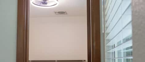 A narrow doorway leading to a room with a bed, a ceiling light, and a vent.