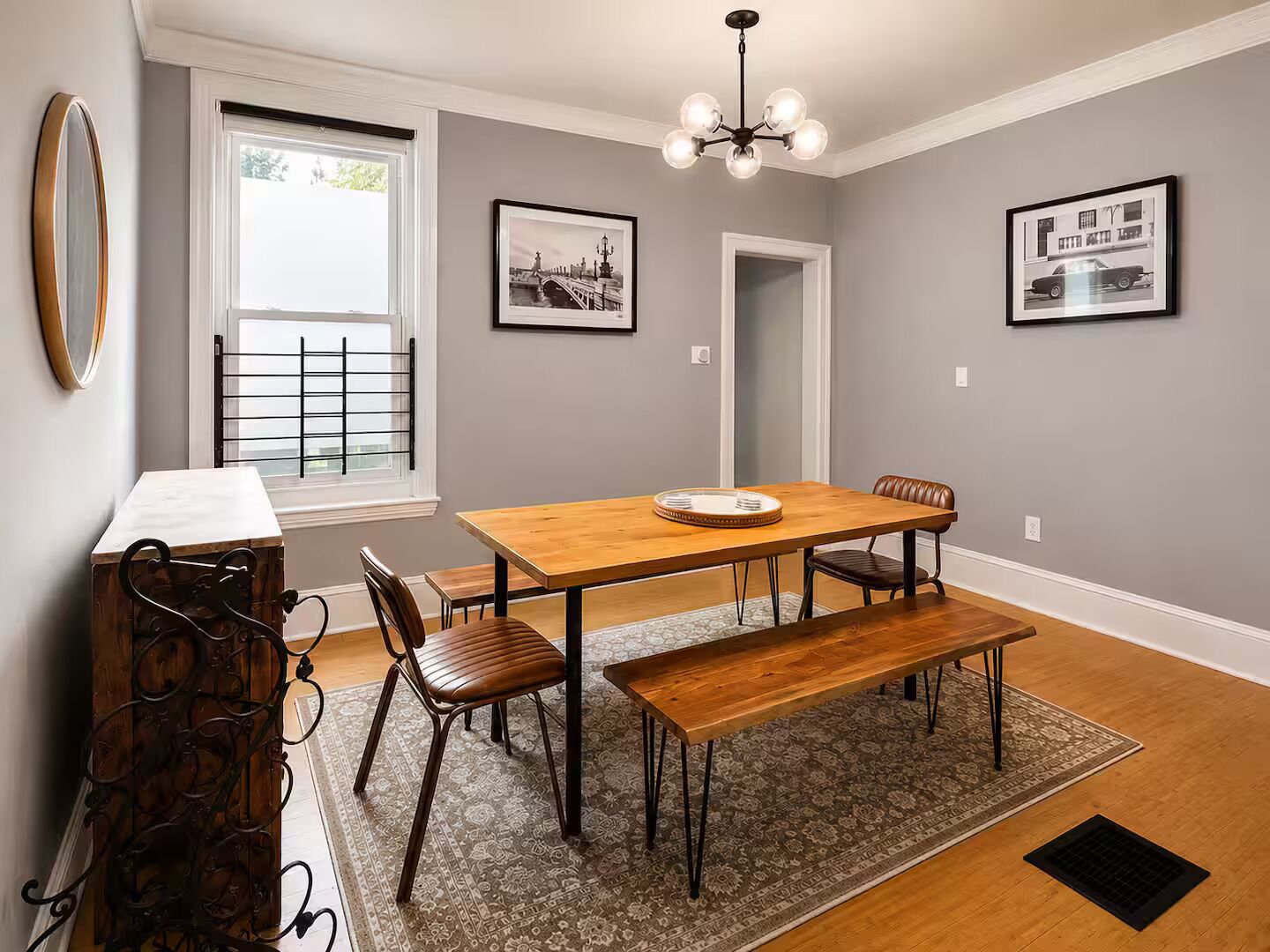 A dining area with a wooden table, four chairs, a bench, a chandelier, and two framed pictures on the wall.