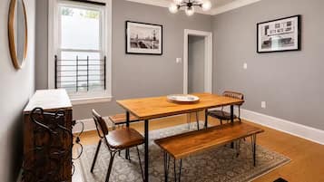 A dining area with a wooden table, four chairs, a bench, a chandelier, and two framed pictures on the wall.