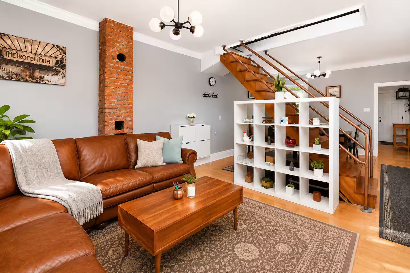 A modern living room with a brown leather sofa, a wooden coffee table, a white shelving unit, and a brick fireplace.
