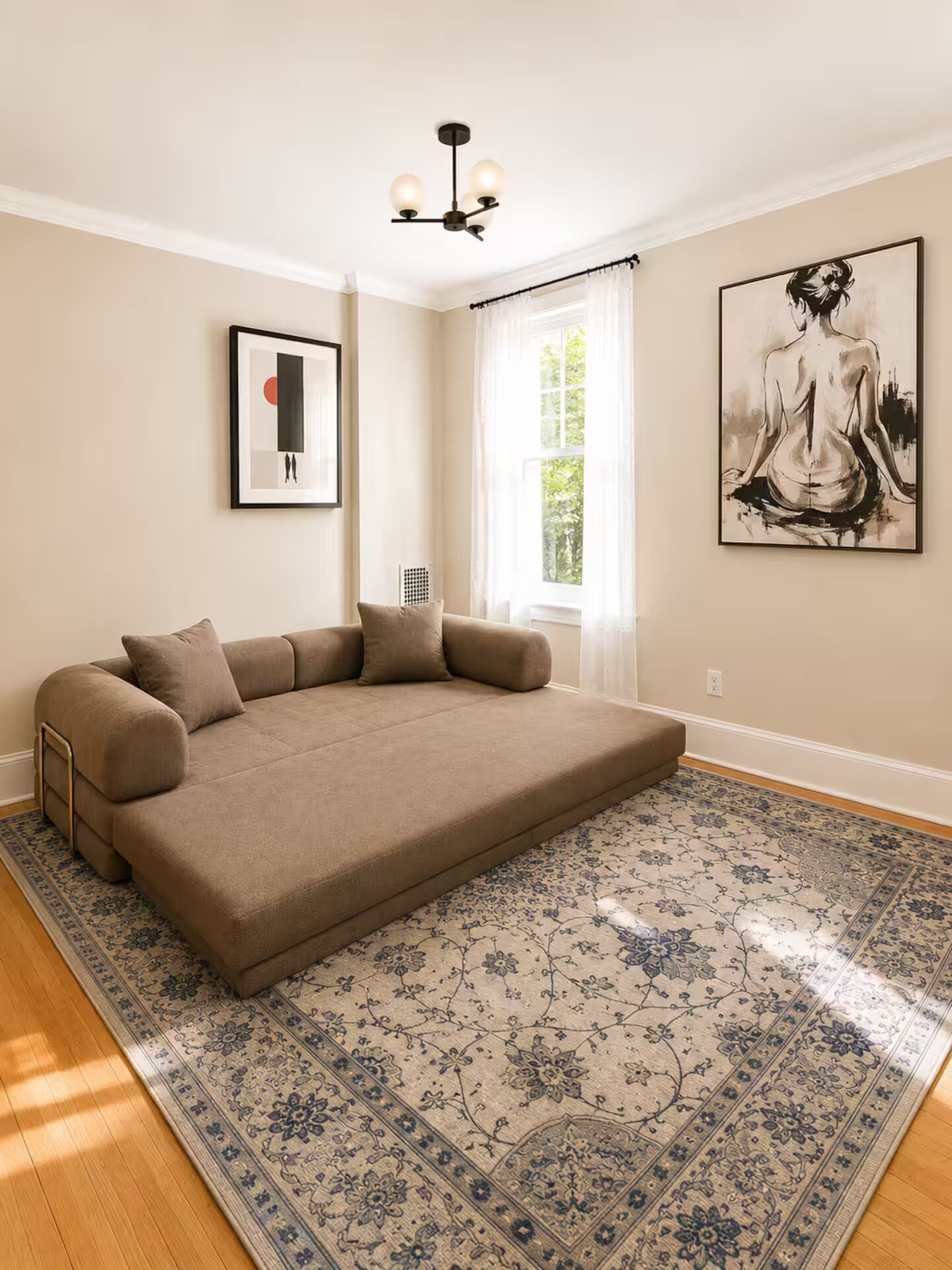 A room with a large sofa, a patterned rug, a ceiling light fixture, and two framed artworks on the walls.
