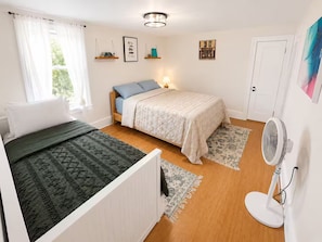 A bedroom with a bed, bedside table, lamp, and a standing fan. - Cozy & Modern Home in University City, Philadelphia (Philadelphia)