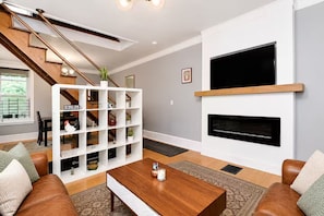 A modern living room with a fireplace, a staircase, and a white shelving unit. - Cozy & Modern Home in University City, Philadelphia (Philadelphia)