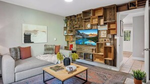 A living room with a sofa, coffee table, and a wall-mounted TV. There is a door leading to another room. - Meadowview Retreat – 3BR/3BA, Hot Tub, Ski Shuttle, East Vail (Vail)