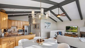 A modern kitchen with wooden cabinets, a dining area with a round table, and a living room with a sofa and a flat-screen TV. - Meadowview Retreat – 3BR/3BA, Hot Tub, Ski Shuttle, East Vail (Vail)