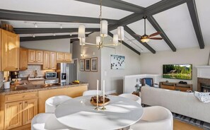 Eine moderne Küche mit Holzausstattung, eine Essecke mit rundem Tisch und ein Wohnzimmer mit Sofa und Flachbildfernseher.