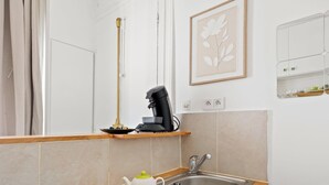 Una cocina con cafetera, un lavabo y una obra de arte floral enmarcada en la pared.