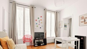 Una sala de estar moderna con un televisor de pantalla plana, una mesa de comedor con sillas, una butaca roja y un sofá con cojines.
