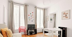Ein modernes Wohnzimmer mit einem Flachbildfernseher, einem Esstisch mit Stühlen, einem roten Sessel und einer Couch mit Kissen.