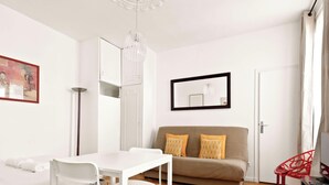 Una sala de estar moderna con un sofá blanco, una mesa de comedor con sillas, una butaca roja y un cuadro en la pared.