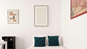 Una habitación con una cama, dos almohadas, una obra de arte abstracta enmarcada y un estante con adornos.