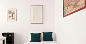 Ein Zimmer mit einem Bett, zwei Kissen, einem gerahmten abstrakten Kunstwerk und einem Regal mit Dekoration.