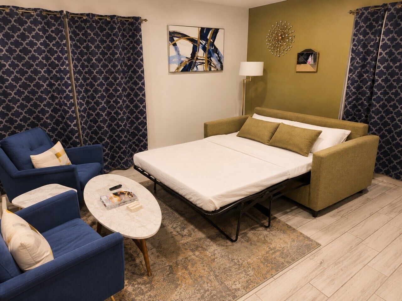 A room with a bed, two armchairs, a small round table, and a lamp.