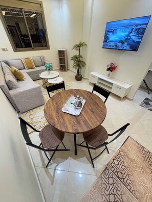 A living room with a round wooden table, black chairs, a grey sofa, a TV mounted on the wall, and a potted plant. - Lovely 2-bedroom apartment in Marrakesh with air conditioning (Marrakesh)