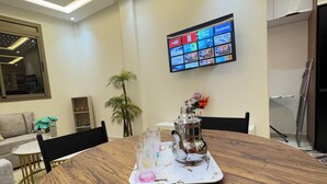 Ein moderner Essbereich mit einem runden Holztisch, einem an der Wand montierten Fernseher und einer Topfpflanze.