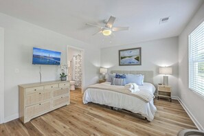Ein Schlafzimmer mit Bett, Nachttischen, Deckenventilator, Fernseher und Kunstwerken an den Wänden.