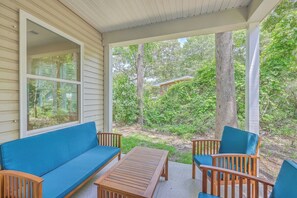 Eine überdachte Veranda mit Holztisch und -stühlen, einer blauen gepolsterten Bank und Blick auf ein bewaldetes Gebiet.