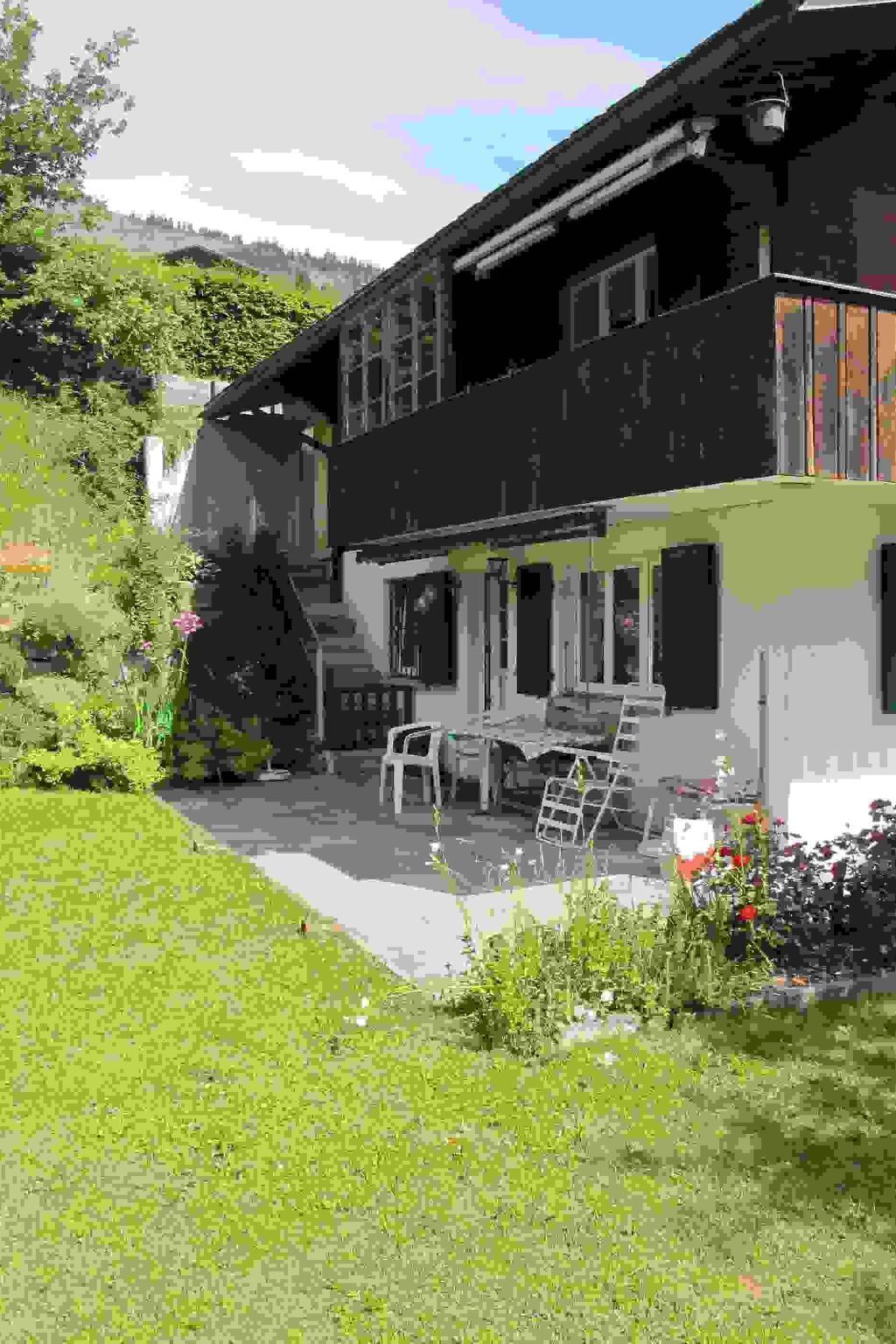 A two-story house with a patio area, outdoor furniture, and a garden.
