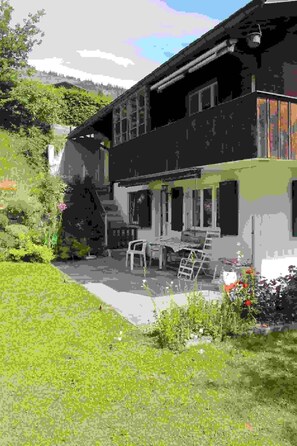Ein zweistöckiges Haus mit einer Terrasse, Gartenmöbeln und einem Garten.