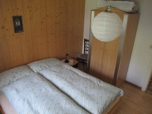Um quarto com uma cama, um guarda-roupa de madeira, uma cadeira e uma pequena mesa.