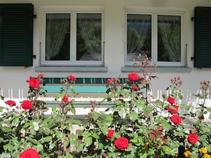 A building with two windows, a bench, and a row of red roses in front. - Helene Appartement/Fewo, Dusche, WC, 2 Schlafräume 3-Zimmerwohnung Parterre by Interhome (Adelboden)