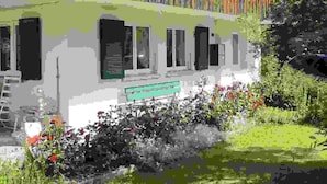Een gebouw met twee verdiepingen, een balkon, een tuin met bloemen en een bank.